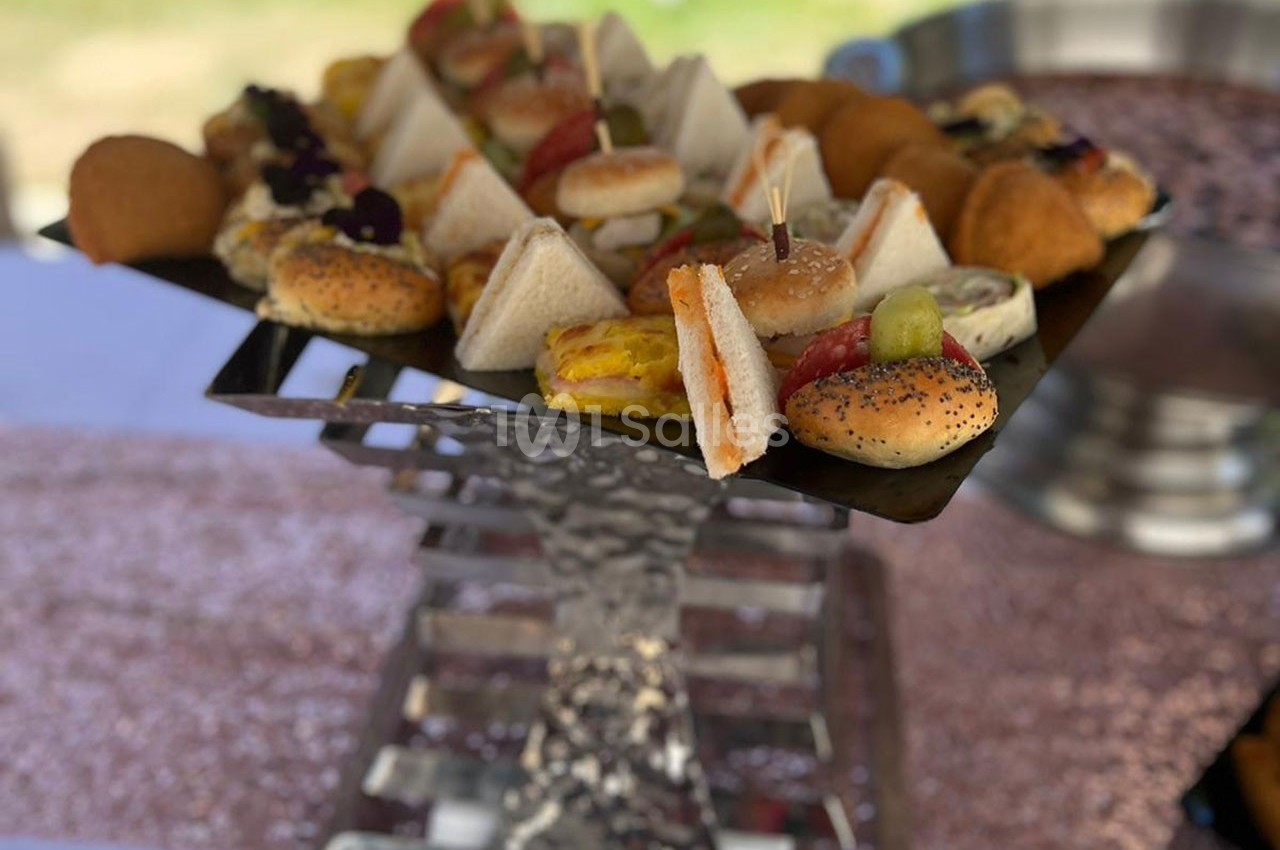 Plateau de mini-sandwichs et amuse-bouches variés disposés sur un présentoir métallique lors d’un événement en extérieur.