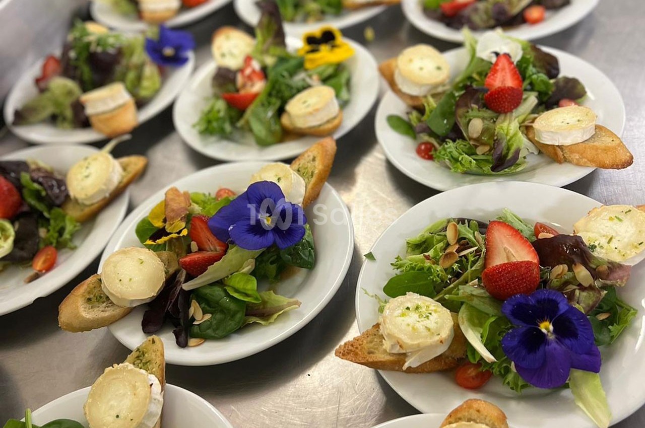 Assiettes de salades garnies de fromage de chèvre sur toast, fraises, fleurs comestibles et graines.