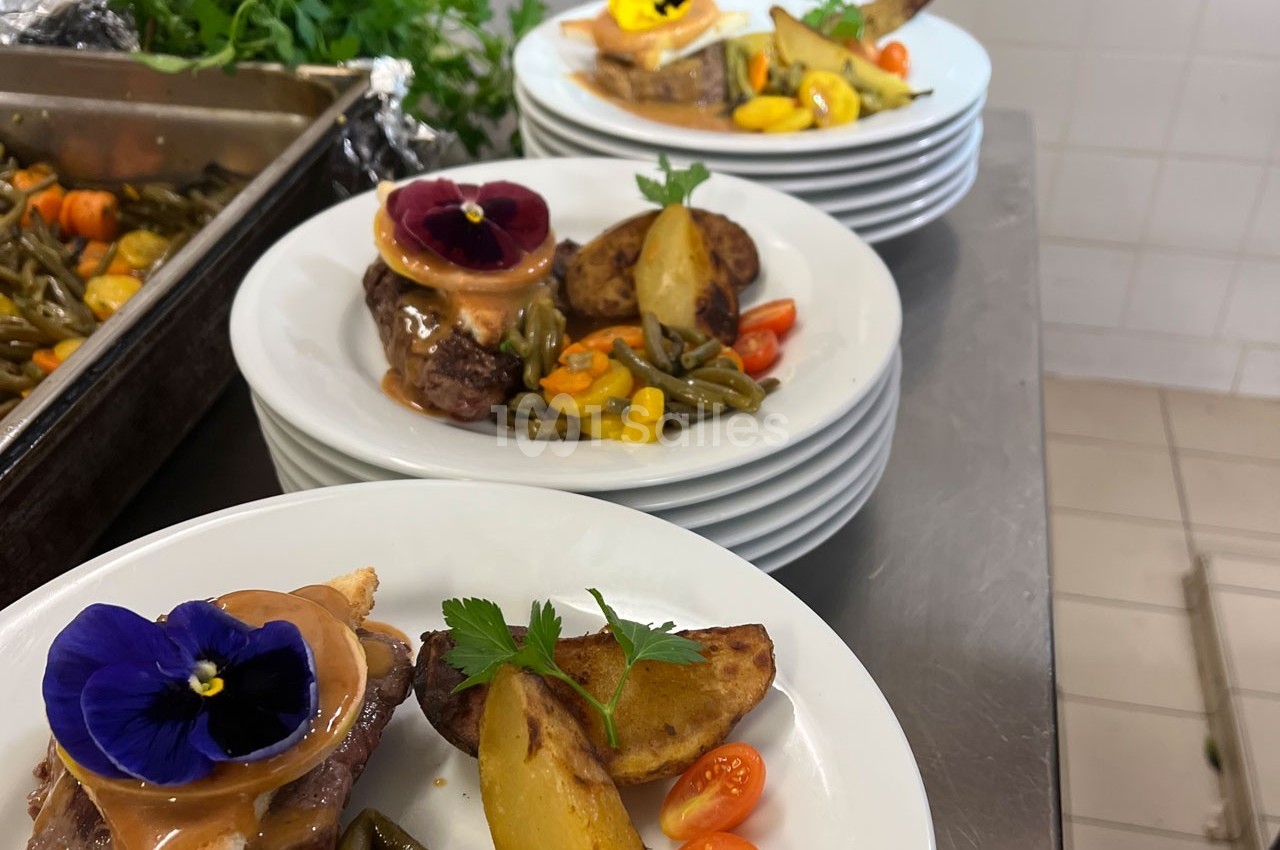 Assiettes dressées avec viande, légumes, pommes de terre rôties et fleurs comestibles dans une cuisine professionnelle.