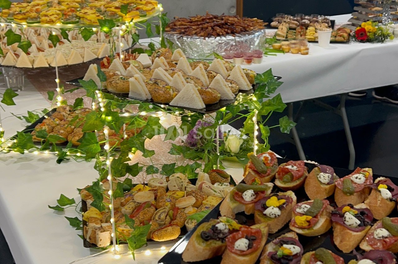 Plateaux de canapés variés et décorés, disposés sur des présentoirs ornés de guirlandes lumineuses et de feuillage.