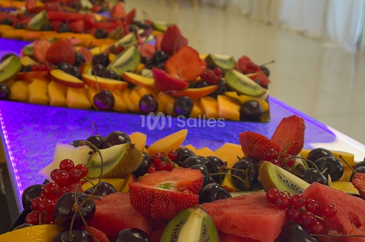 Plateaux de fruits frais variés comprenant pastèque, fraises, kiwis, cerises et groseilles, disposés sur une table lumineuse.