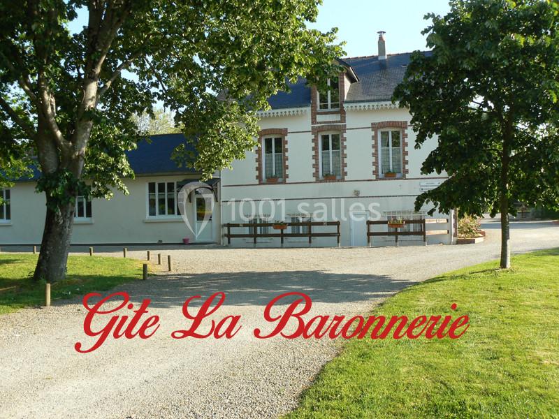Façade d'un gîte rural entouré d'arbres, avec une allée gravillonnée et l'inscription ’Gîte La Baronnerie’.