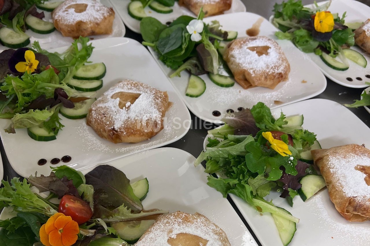 Assiettes de pastillas saupoudrées de sucre glace, accompagnées de salade verte, légumes frais et fleurs comestibles.