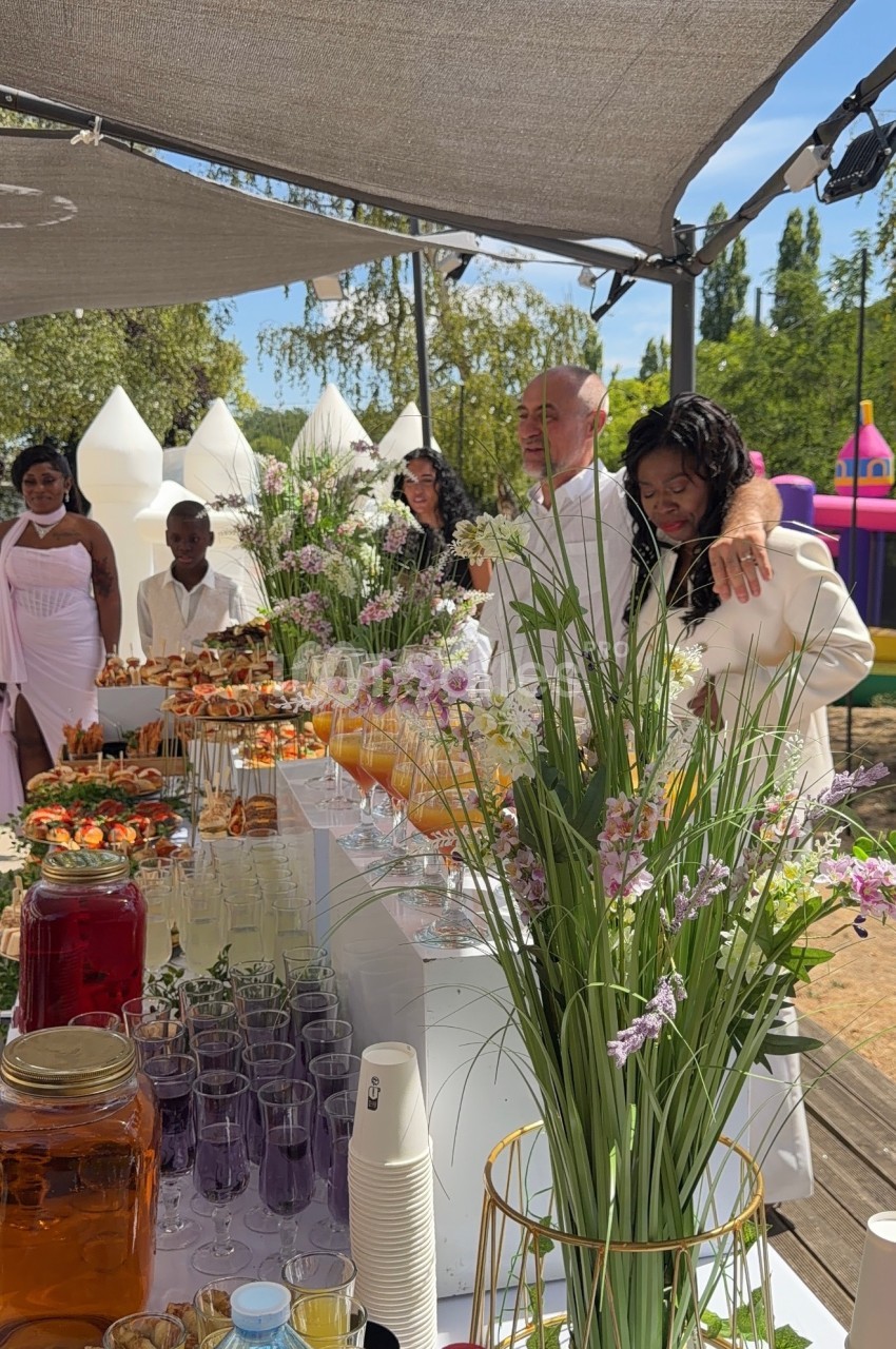 Table garnie de boissons et de plats colorés lors d'une réception en plein air, avec des invités en arrière-plan.