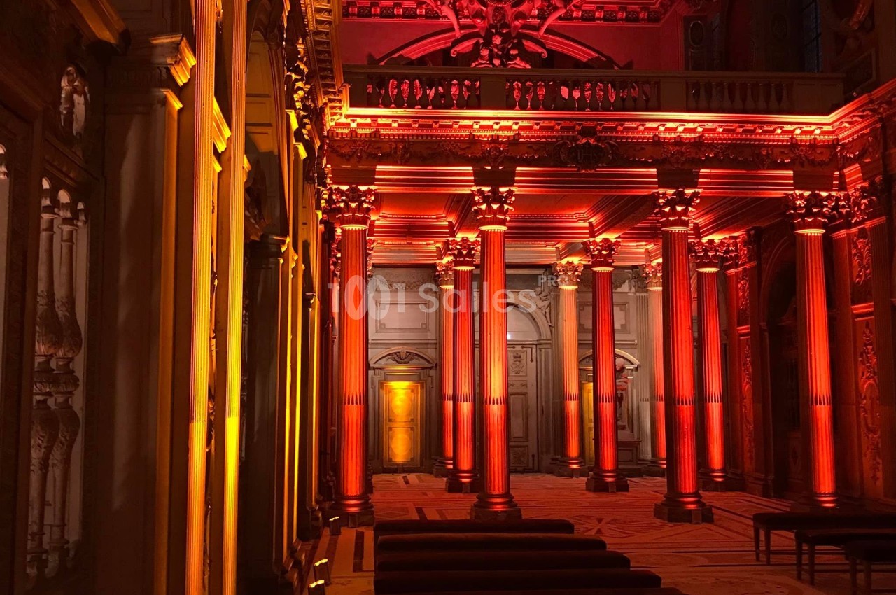 Colonnes illuminées en orange et rouge dans une salle ornée de détails architecturaux et de sculptures.