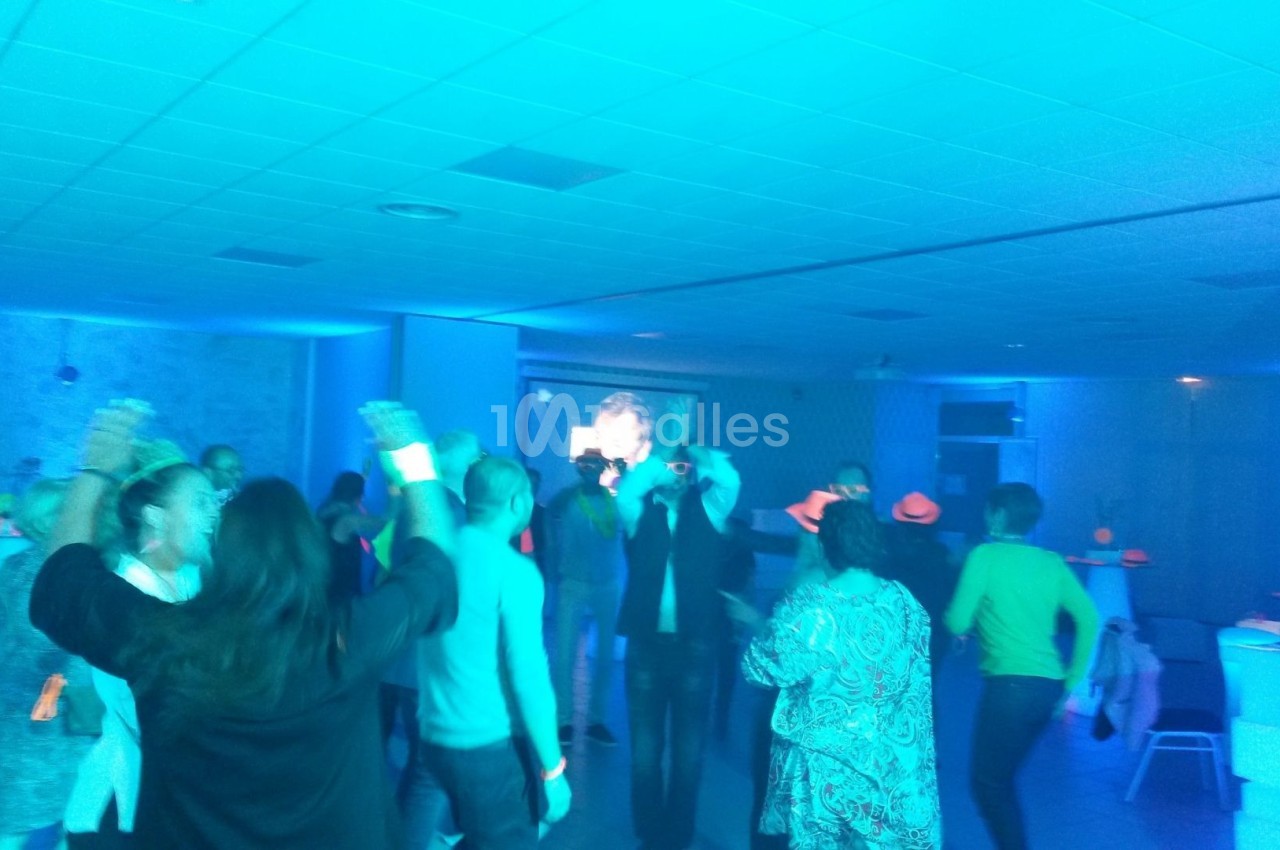 Des personnes dansent dans une salle éclairée par une lumière bleue, avec des accessoires lumineux.