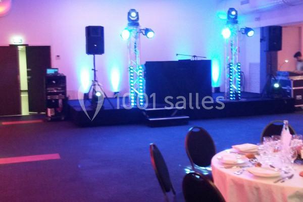 Scène éclairée avec des projecteurs bleus, équipée de matériel audio, dans une salle avec tables dressées.