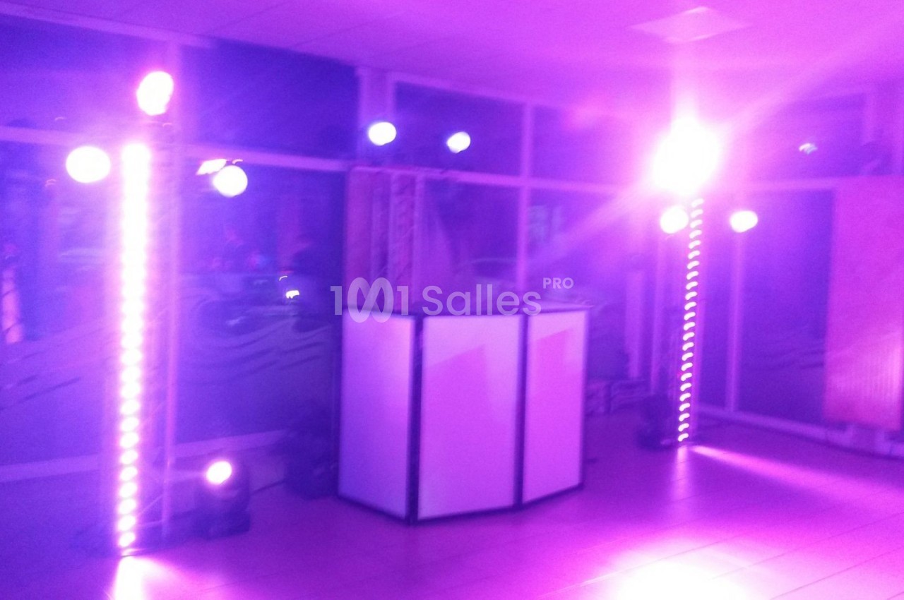 Éclairage violet avec projecteurs et colonnes lumineuses autour d'une console blanche dans une salle.