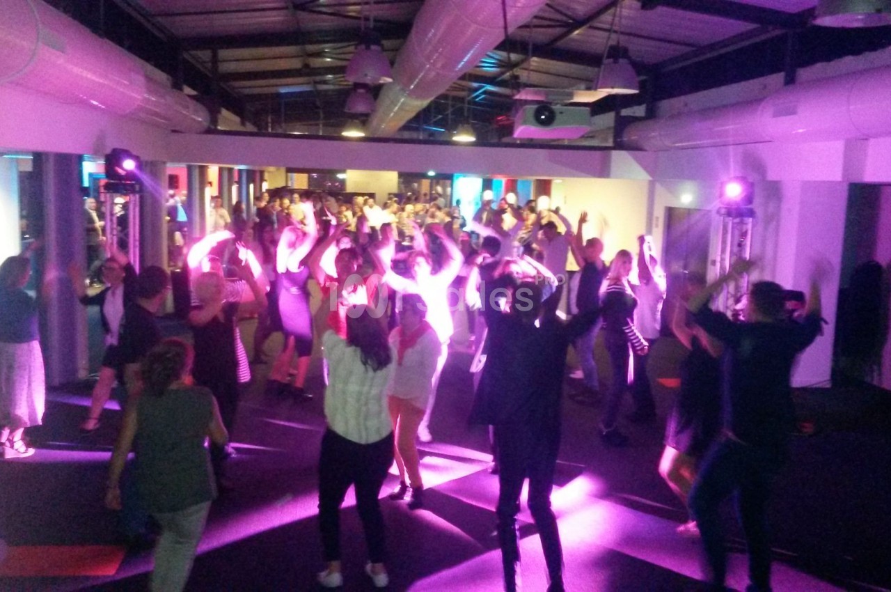 Groupe de personnes dansant sous des lumières colorées dans une salle avec un plafond industriel.