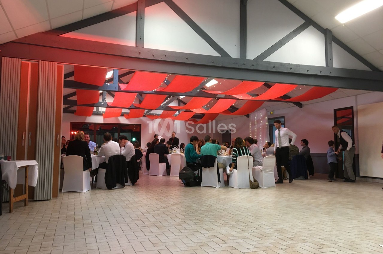 Salle de réception avec des invités assis à des tables rondes, sous un plafond décoré de bandes rouges.