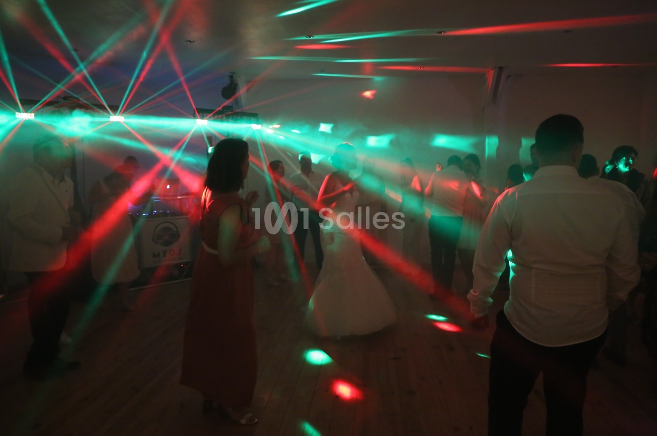 Des invités dansent dans une salle sombre illuminée par des faisceaux lumineux rouges et verts.
