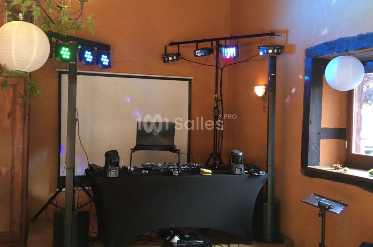 Installation de matériel de DJ avec table de mixage, projecteurs lumineux et écran dans une salle aux murs orange.