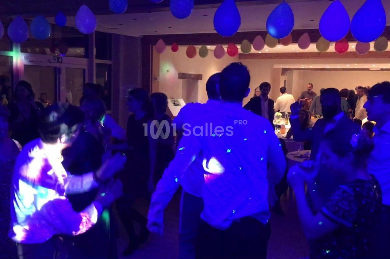 Des personnes dansent dans une salle décorée de ballons, éclairée par des lumières colorées.