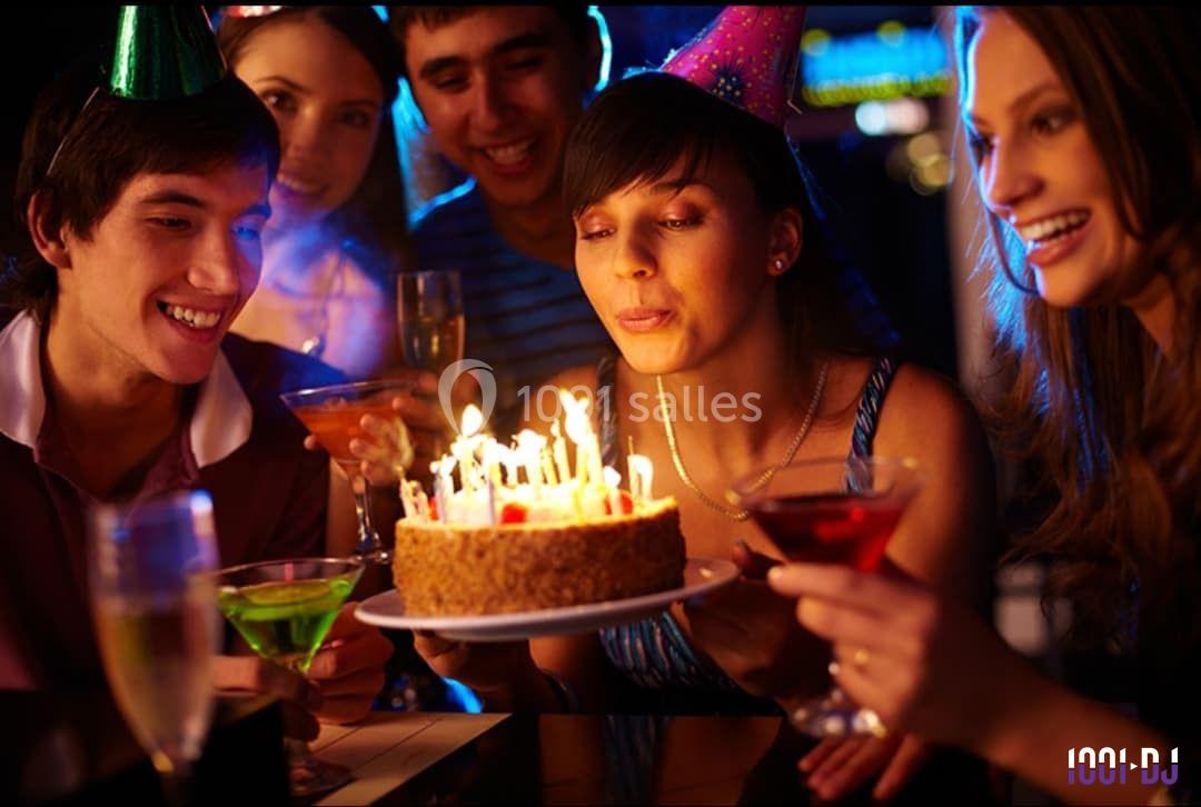 Une femme souffle les bougies d'un gâteau d'anniversaire entourée d'amis tenant des verres dans une ambiance festive.
