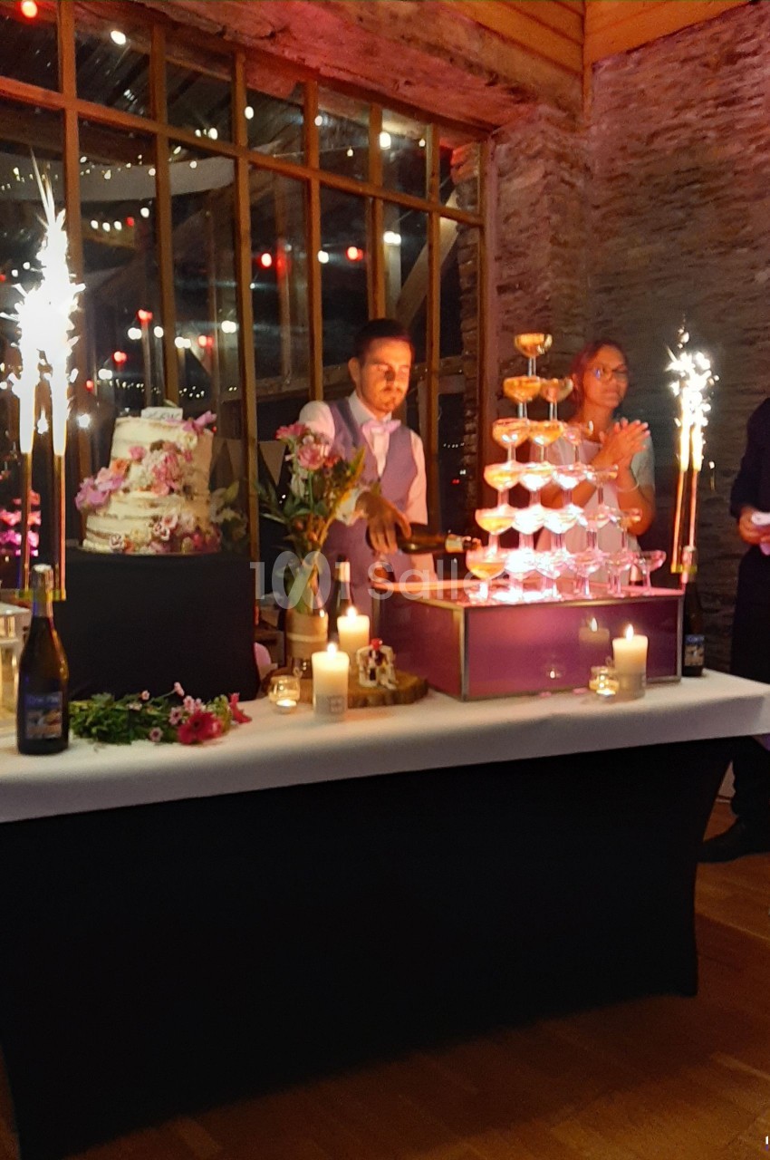 Un homme remplit une pyramide de verres avec du champagne lors d'une réception festive, entouré de décorations lumineuses.
