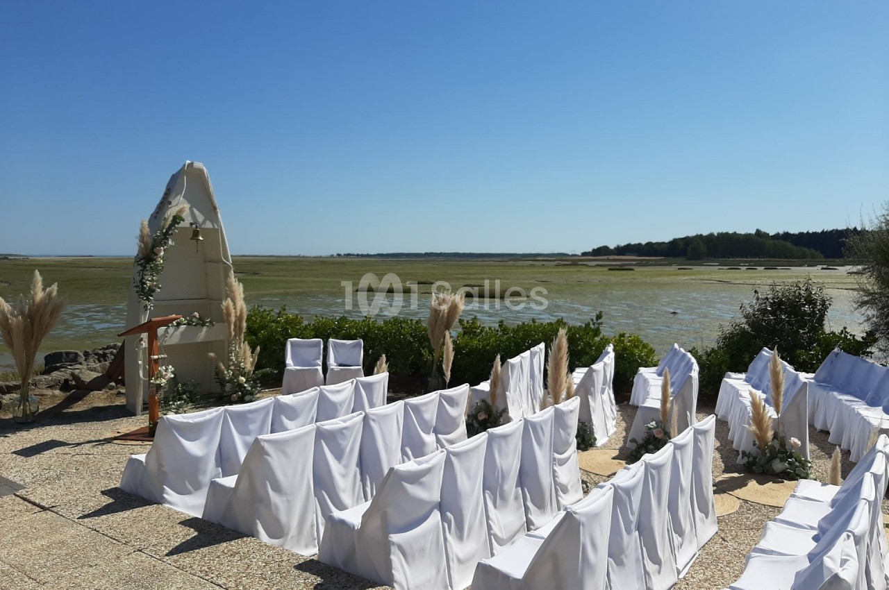 Chaises blanches alignées pour une cérémonie en plein air, avec vue sur un paysage de marais sous un ciel dégagé.