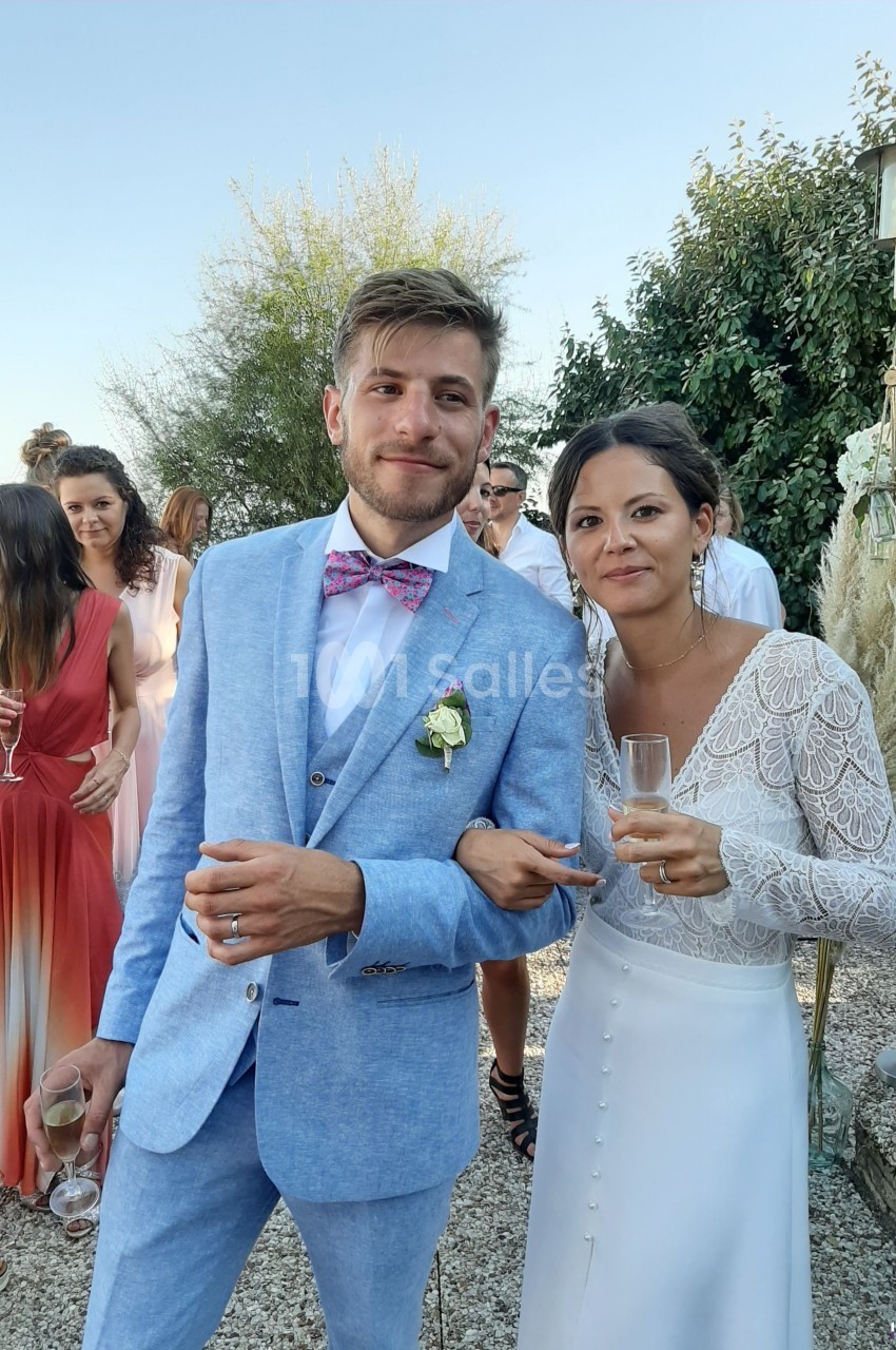 Un couple habillé élégamment, tenant des verres, pose en extérieur lors d'un événement festif.