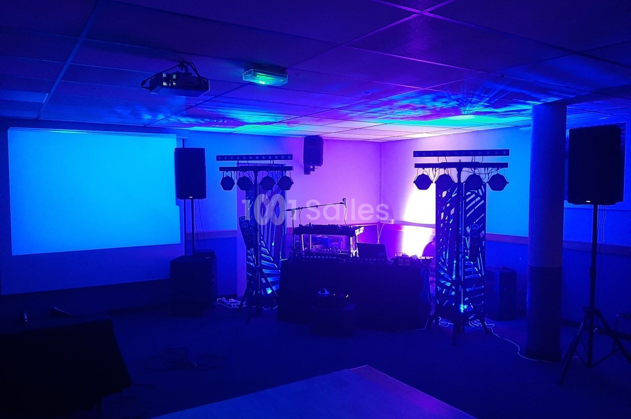 Salle équipée pour un événement avec éclairage coloré, projecteurs, enceintes et matériel audio sur scène.
