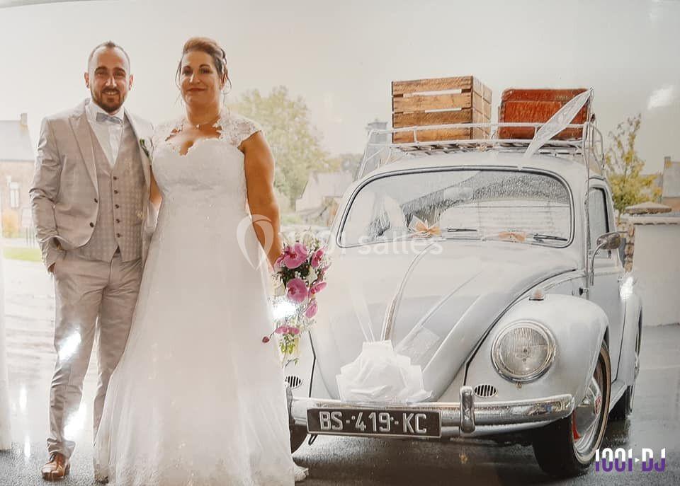 Un couple en tenue de mariage pose devant une voiture ancienne décorée pour l'occasion.