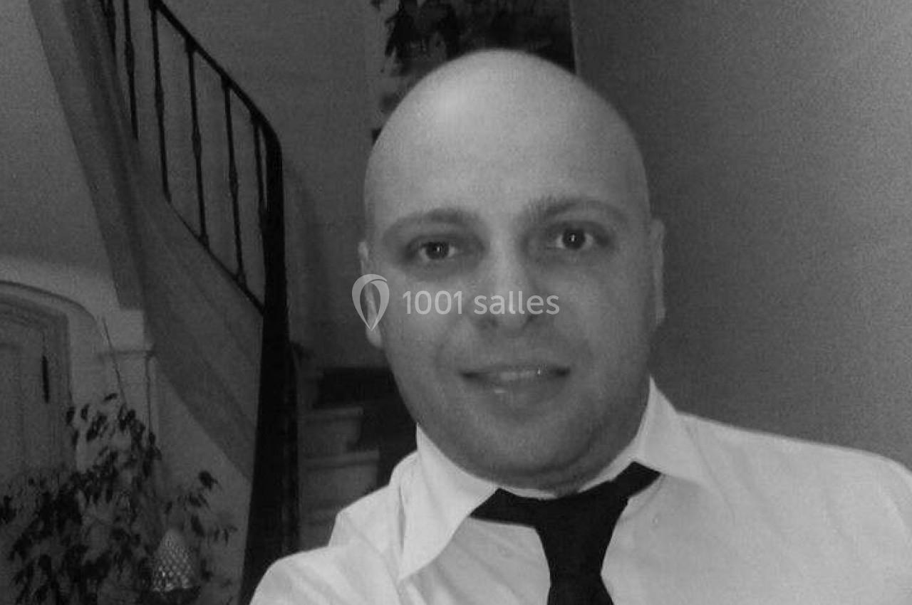 Homme en chemise et cravate prenant un selfie dans un intérieur avec un escalier en colimaçon en arrière-plan.