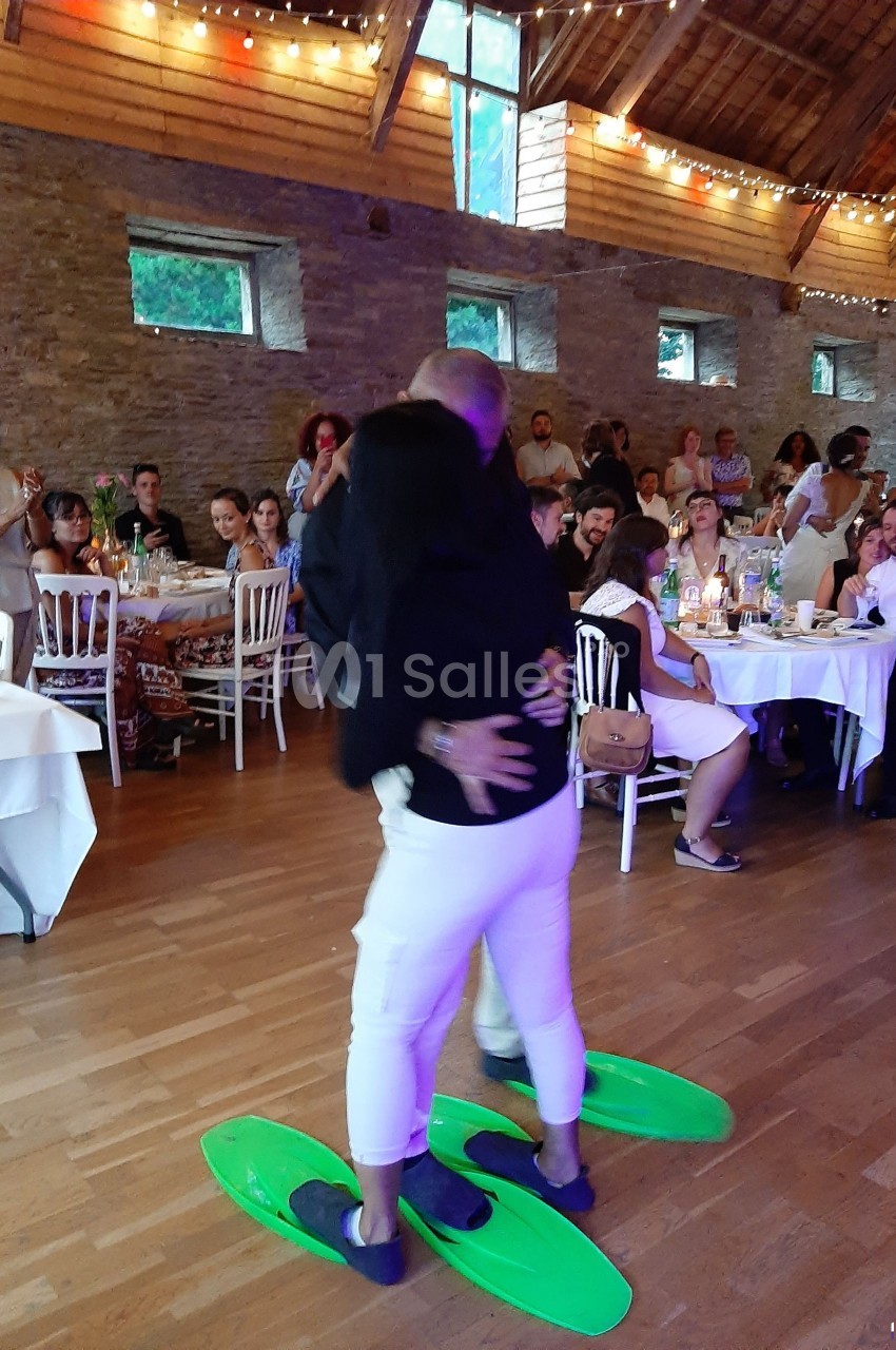 Un couple danse sur une piste en bois, portant des palmes vertes, devant des invités assis dans une salle décorée.