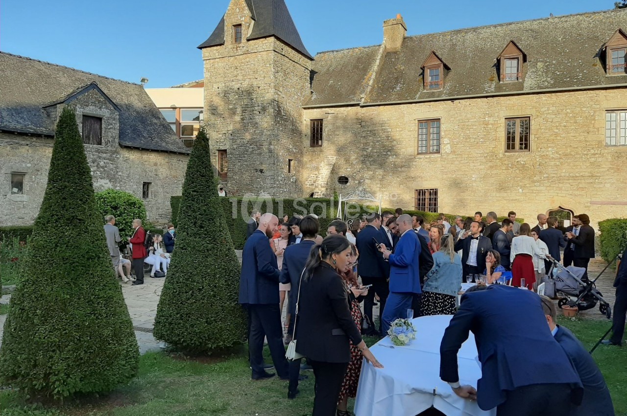 Groupe de personnes rassemblées dans la cour d'un bâtiment en pierre historique, lors d'un événement en plein air.