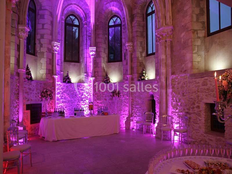 Salle en pierre avec éclairage violet, tables décorées et buffet dressé, ambiance élégante et festive.