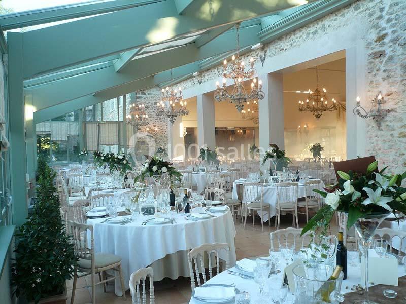Salle de réception lumineuse avec tables rondes dressées, décorée de fleurs et éclairée par des lustres élégants.