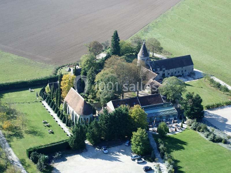 Vue aérienne d'un domaine rural avec une église, des bâtiments anciens, des arbres et des champs environnants.