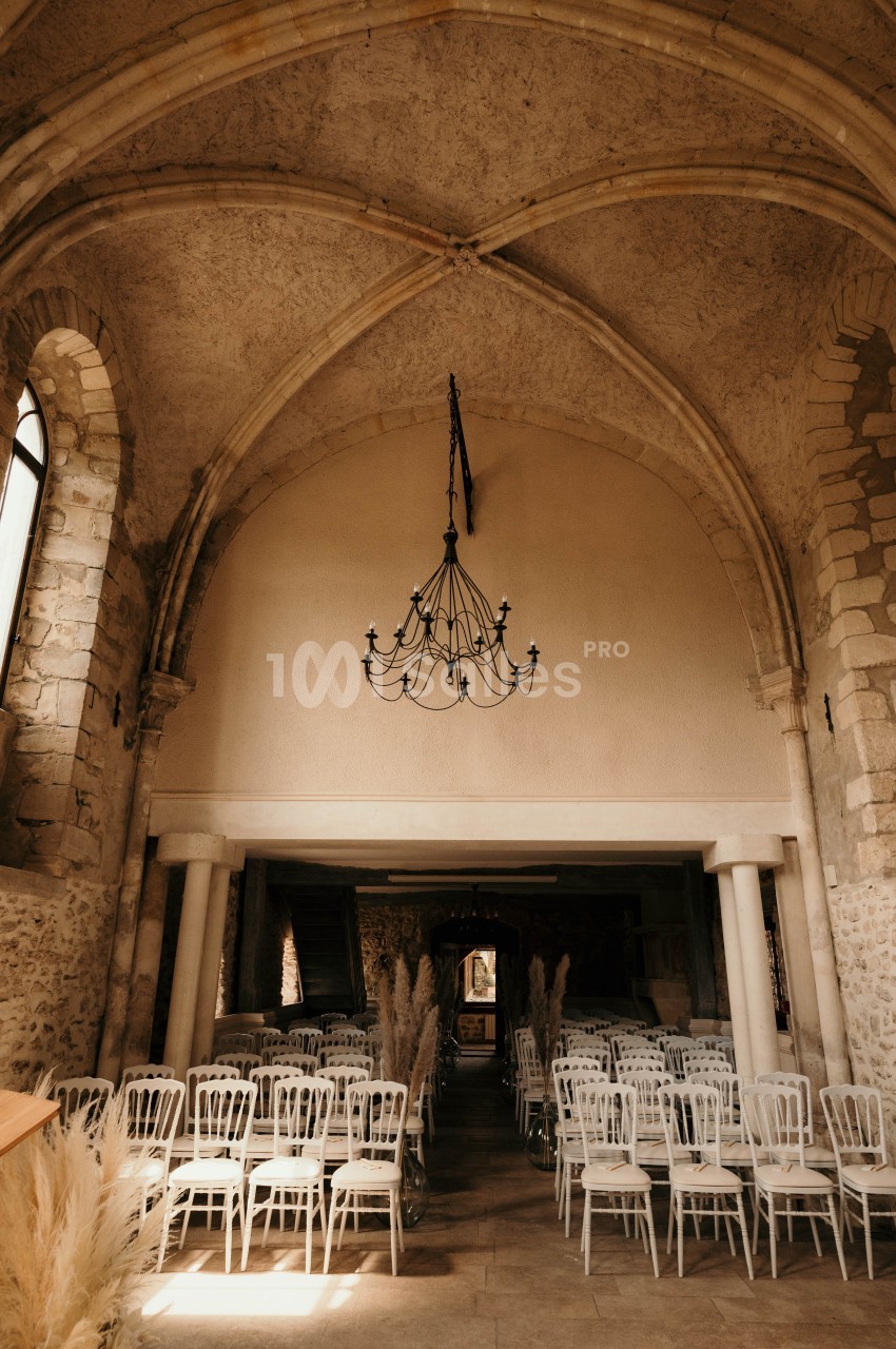 Intérieur d'une ancienne église avec des voûtes en pierre, des chaises blanches alignées et un lustre suspendu.