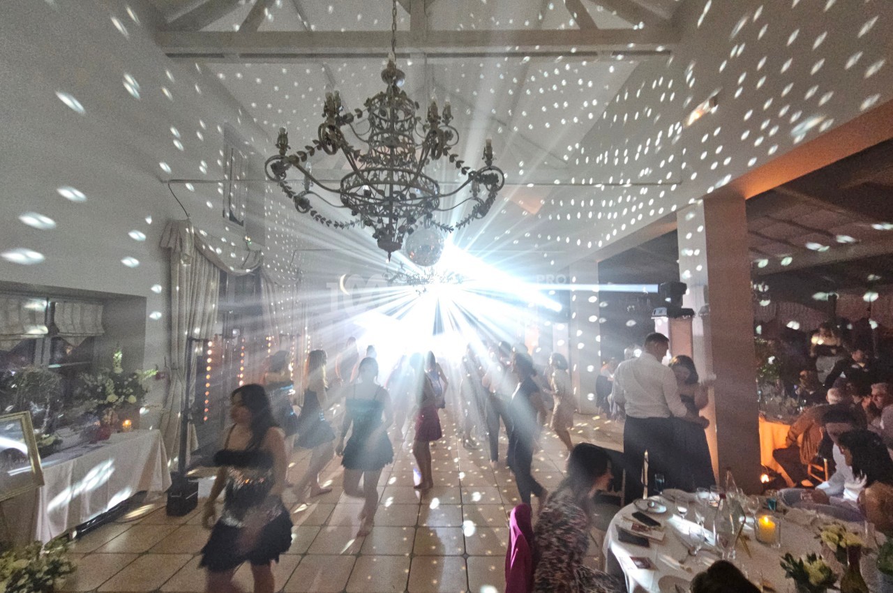 Salle de réception avec des invités dansant sous un éclairage festif et un lustre central.