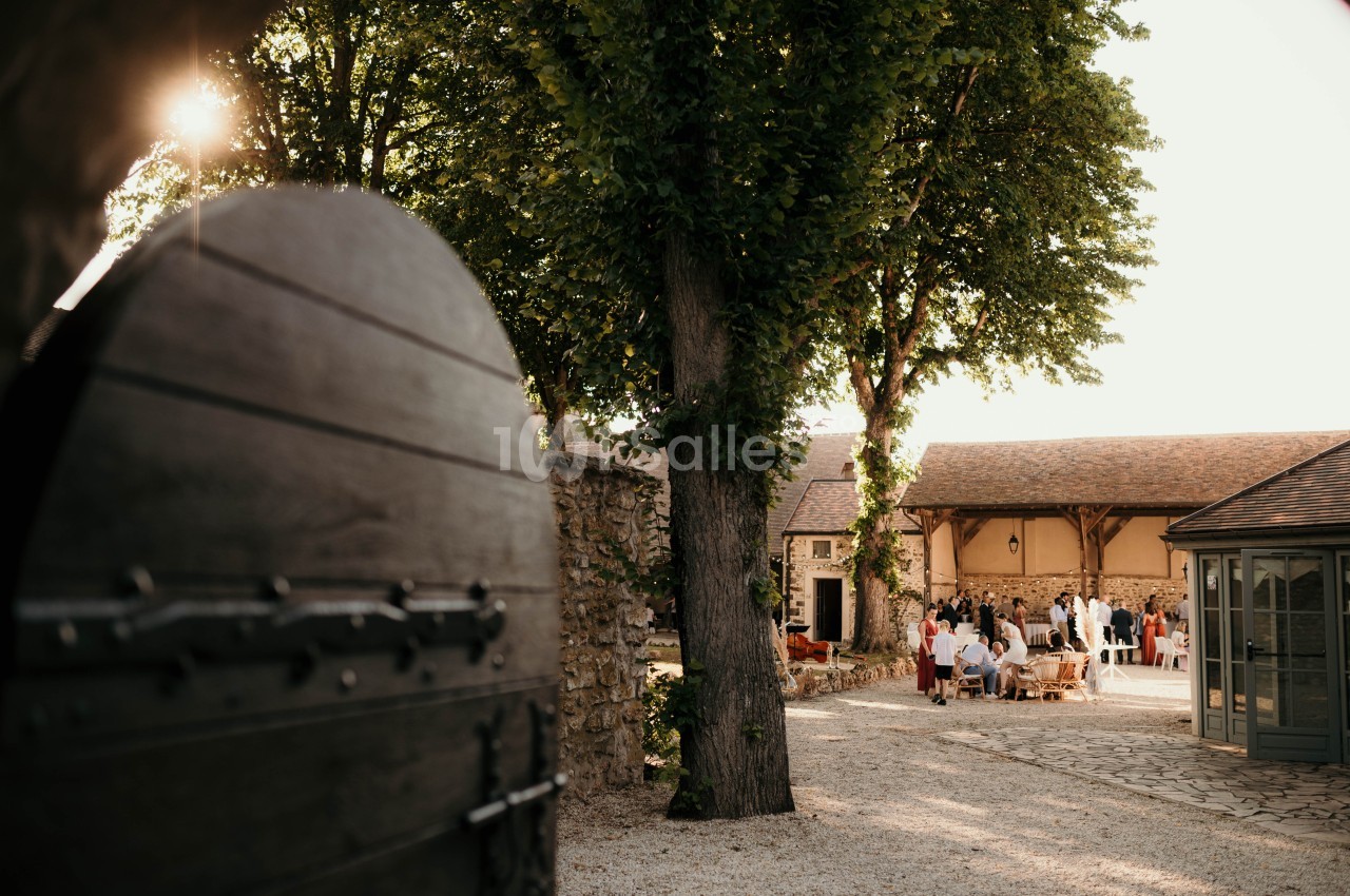 Cour intérieure d'un bâtiment en pierre, avec des invités rassemblés sous des arbres par une journée ensoleillée.