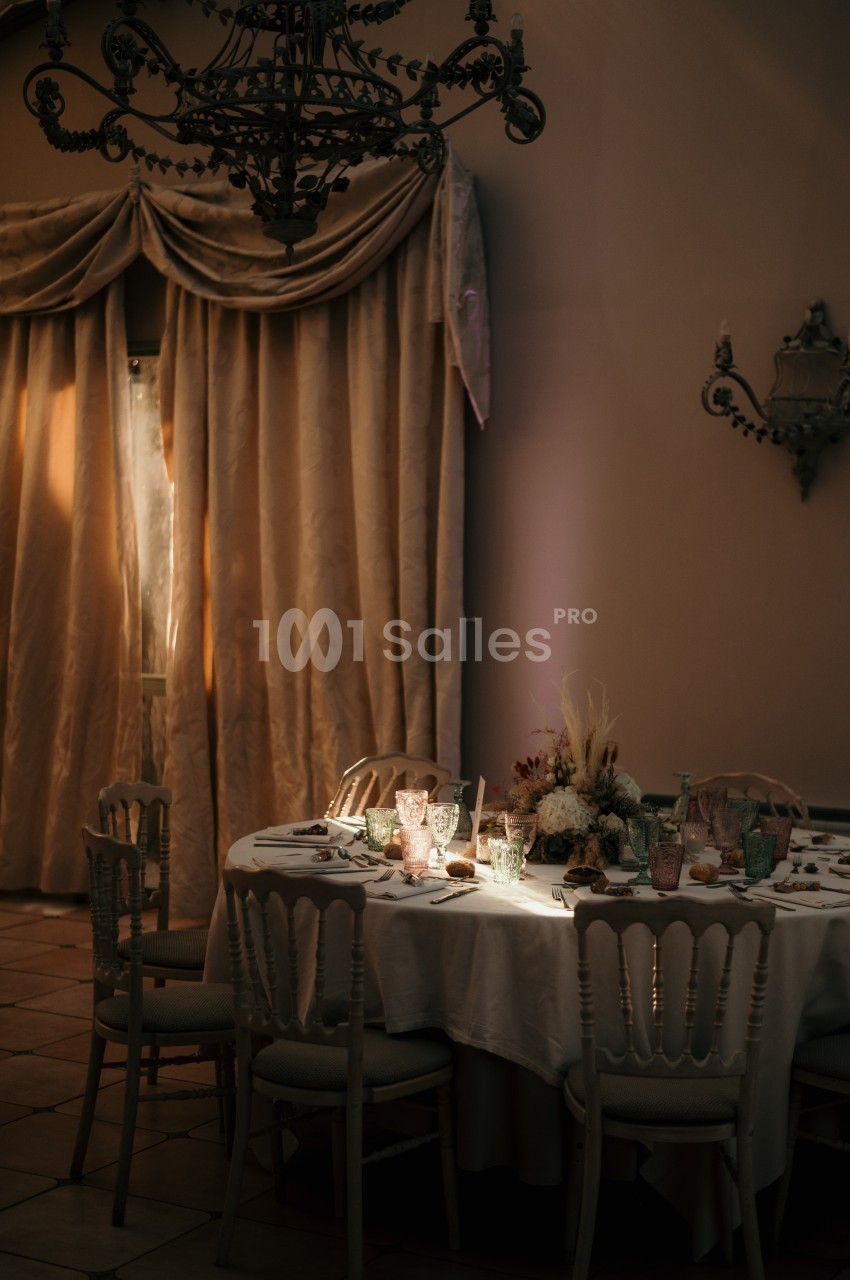 Table ronde élégamment dressée avec des verres colorés et un centre de table floral, éclairée par une lumière tamisée.