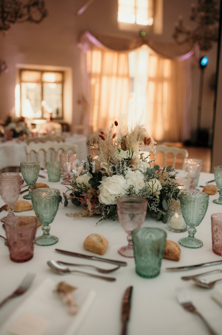 Table dressée avec vaisselle colorée, bouquet floral central, pains individuels et lumière naturelle en arrière-plan.