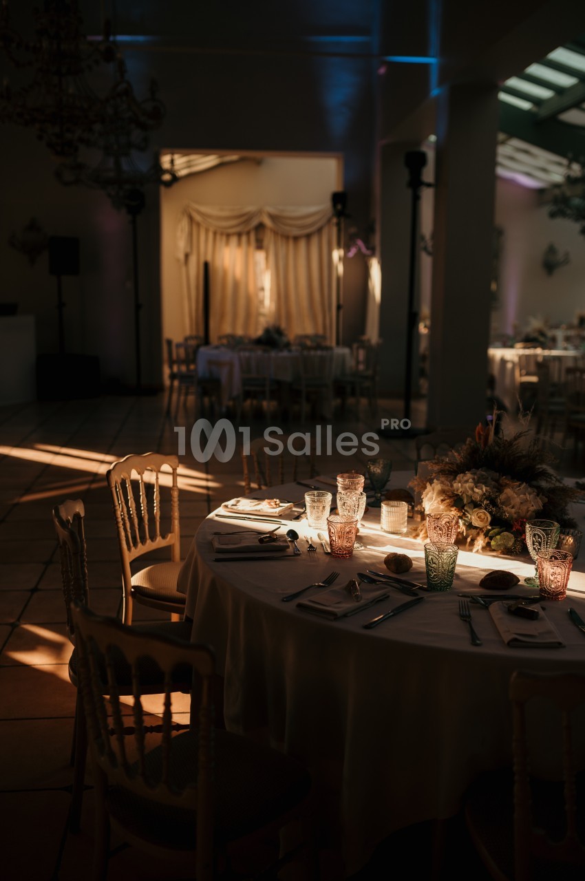 Table dressée avec vaisselle raffinée et décoration florale dans une salle de réception baignée de lumière tamisée.