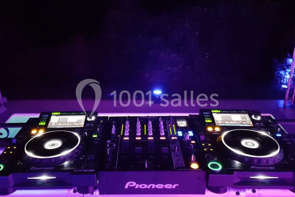 Deux platines DJ et une table de mixage éclairées par des lumières violettes dans un environnement sombre.