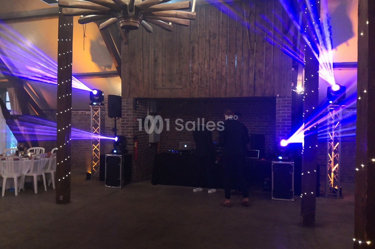 Deux personnes ajustent un équipement de DJ dans une salle décorée avec des lumières colorées et des poutres en bois.
