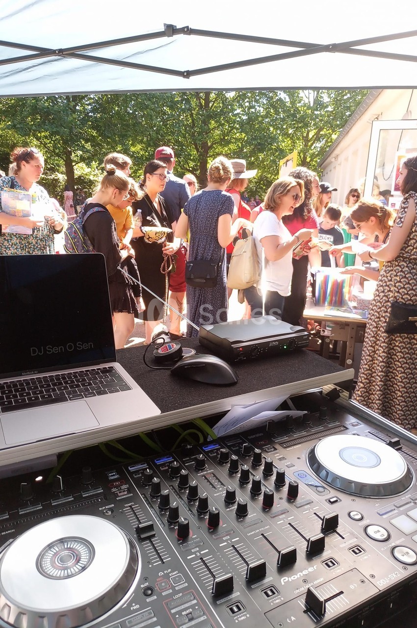 Table de mixage et ordinateur sous une tente, avec des personnes rassemblées autour de stands en arrière-plan.