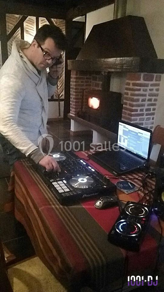 Homme mixant de la musique sur une table de mixage avec un ordinateur portable dans une pièce avec cheminée.