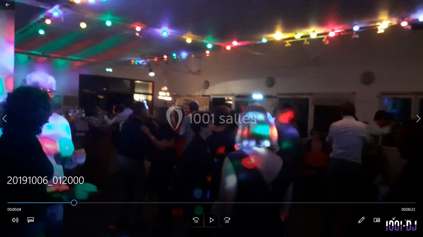 Des personnes dansent dans une salle faiblement éclairée, décorée de guirlandes lumineuses colorées.