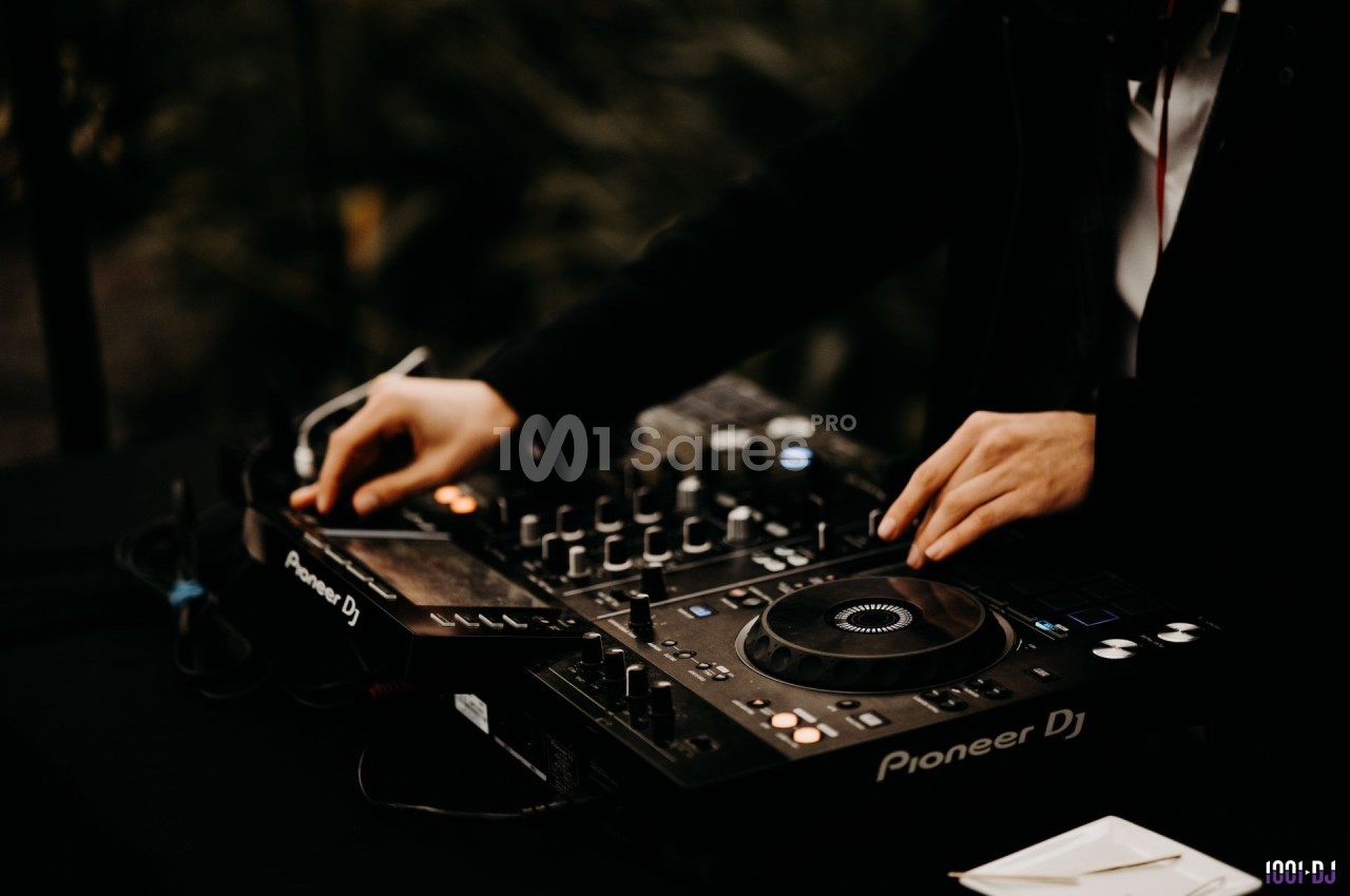 Un DJ manipule une table de mixage et des platines dans un environnement sombre.