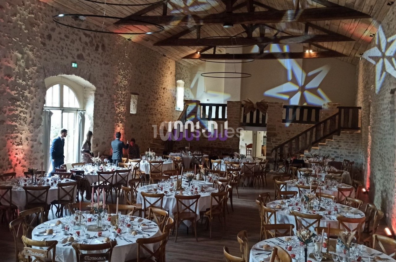 Salle de réception en pierre avec tables dressées pour un événement, éclairages décoratifs en étoile au plafond.