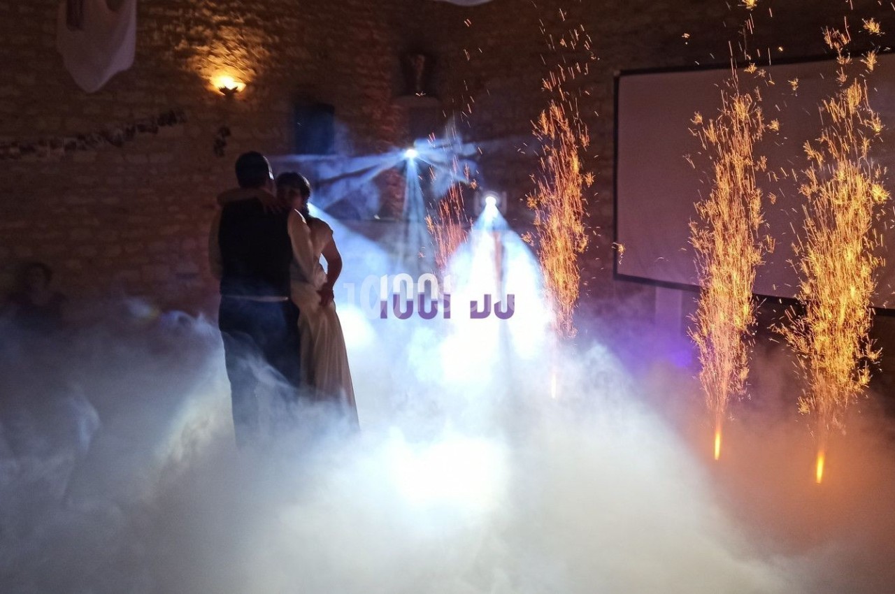 Un couple danse dans une salle sombre éclairée par des étincelles et des effets de fumée.