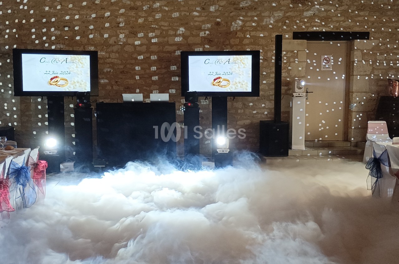 Salle de réception décorée avec des tables dressées, des écrans affichant un menu et un sol recouvert de fumée artificielle.