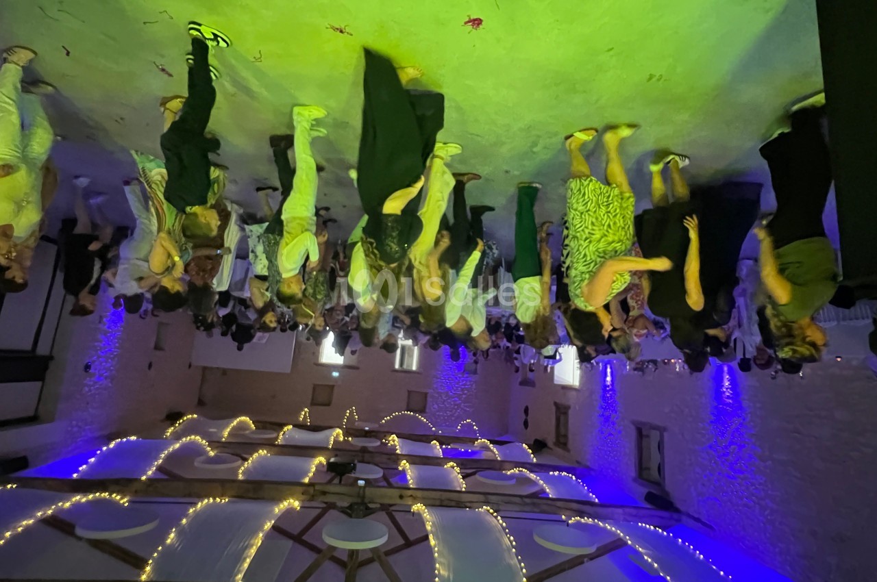 Des personnes dansent dans une salle éclairée par des lumières colorées, avec un plafond décoré de guirlandes lumineuses.