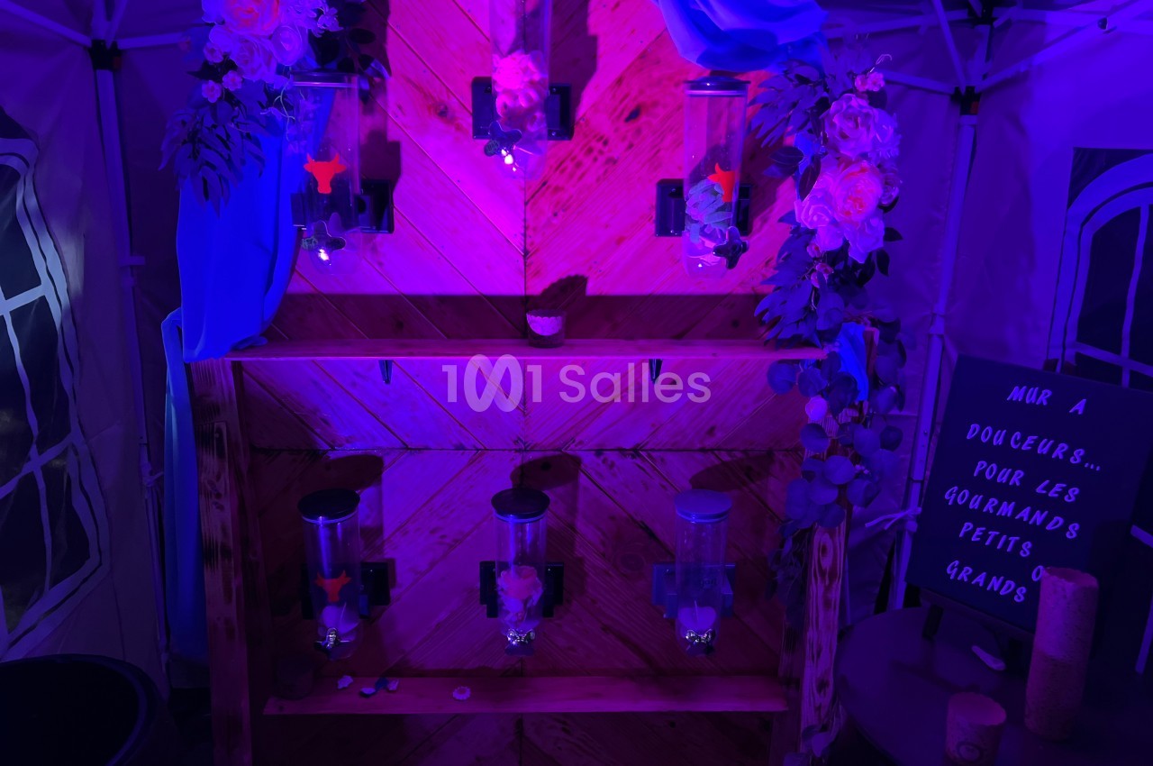Mur de distributeurs de bonbons éclairé par une lumière violette, décoré de fleurs et d'un panneau écrit à la main.