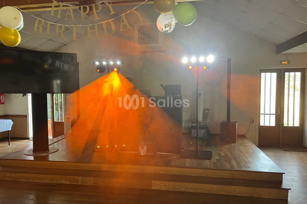Scène décorée pour un anniversaire avec guirlande ’Happy Birthday’, éclairages colorés et fumée orange.