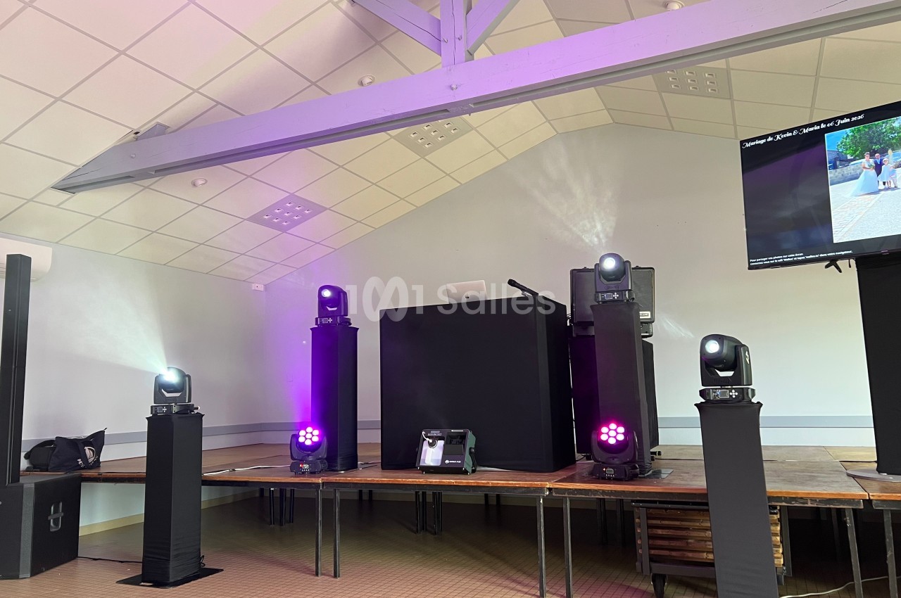 Scène équipée de projecteurs lumineux, d'une table de mixage et d'un écran dans une salle au plafond en pente.