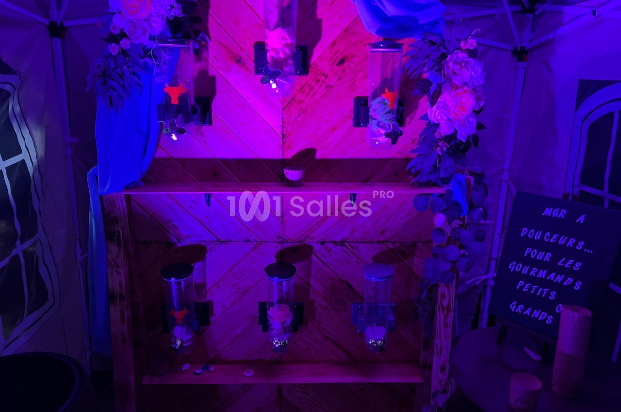 Mur de distributeurs de bonbons éclairé par une lumière violette, décoré de fleurs et d'un panneau écrit à la main.