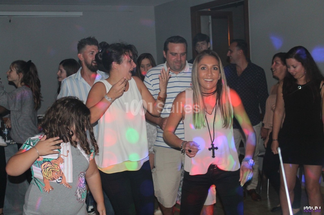 Des personnes dansent et s'amusent dans une salle éclairée par des lumières colorées lors d'une fête.
